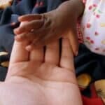 A baby's hand reaching out to someone's hand, highlighting the importance of The Plural Association and Power to the Plurals.