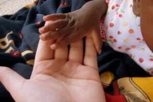 A baby's hand reaching out to someone's hand, highlighting the importance of The Plural Association and Power to the Plurals.